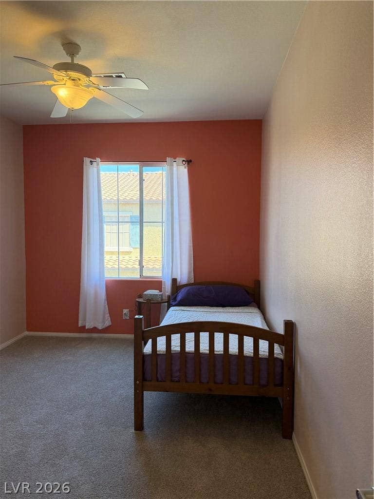 Natural light streams through a large window onto soft carpeting in this cozy bedroom.