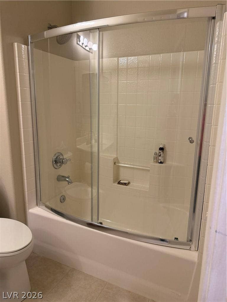 Sliding glass doors enclose a classic tub shower combination framed by neutral tiling.