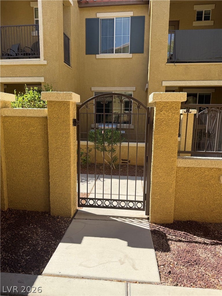 An arched wrought iron gate opens to a private entryway set within stucco walls.