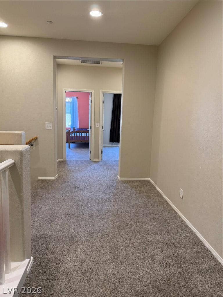Recessed lighting illuminates a carpeted upstairs landing leading toward bedrooms.
