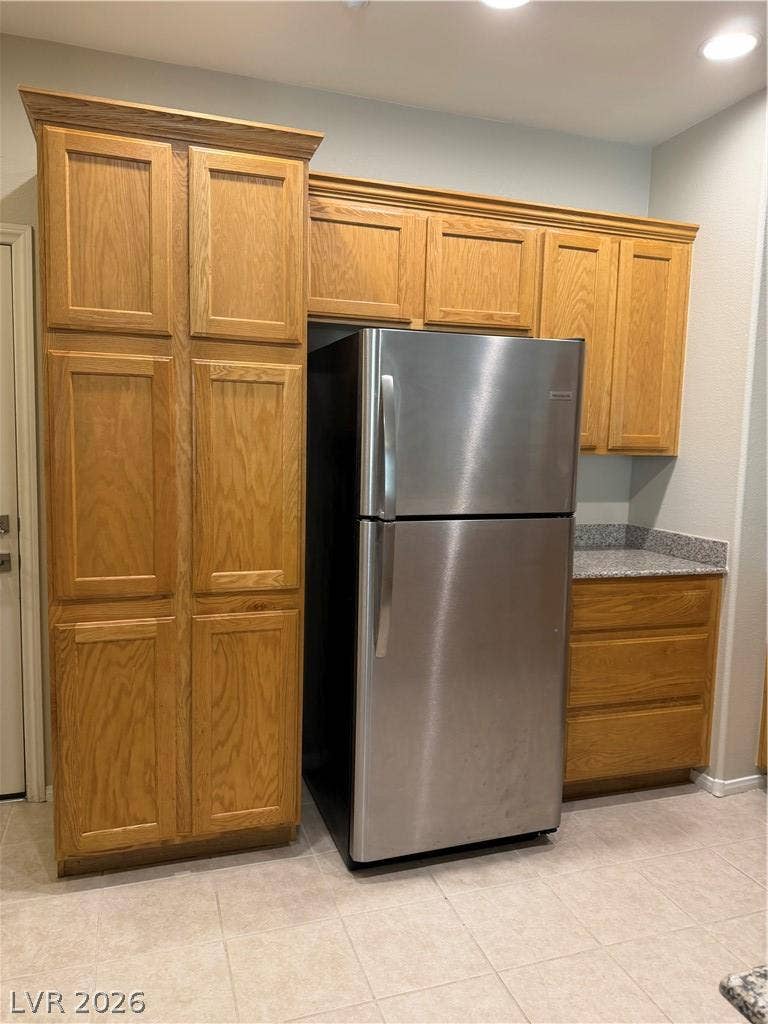 Rich wood cabinetry surrounds a stainless steel refrigerator over durable tiled flooring.