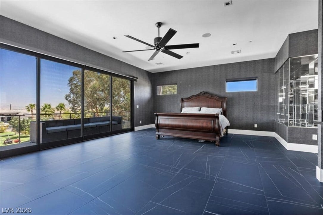 2839 Edgemont Drive, Henderson, NV 89074 A spacious bedroom features floor-to-ceiling windows with balcony access and a grand, dark wood bed frame.
