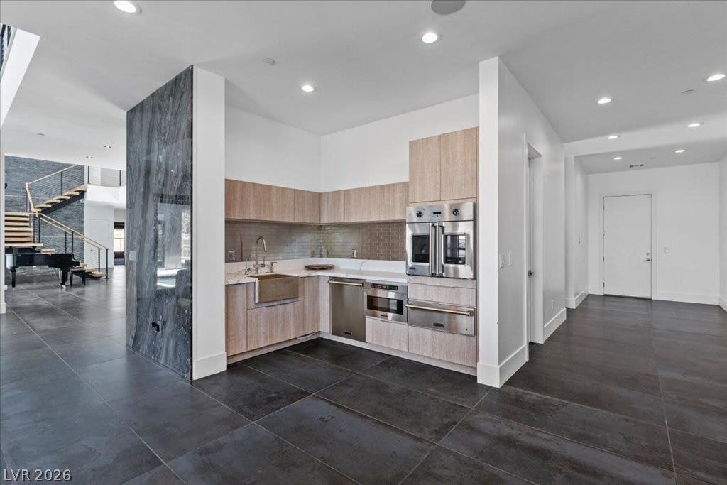 2839 Edgemont Drive, Henderson, NV 89074 A contemporary kitchen space boasts sleek appliances and dark tile flooring, leading to an open living area with a grand staircase.