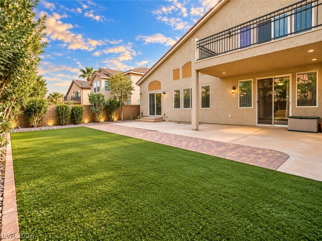 669 Doubleshot Lane, Henderson, NV 89052 An inviting covered patio and balcony overlook a manicured lawn framed by stucco walls.