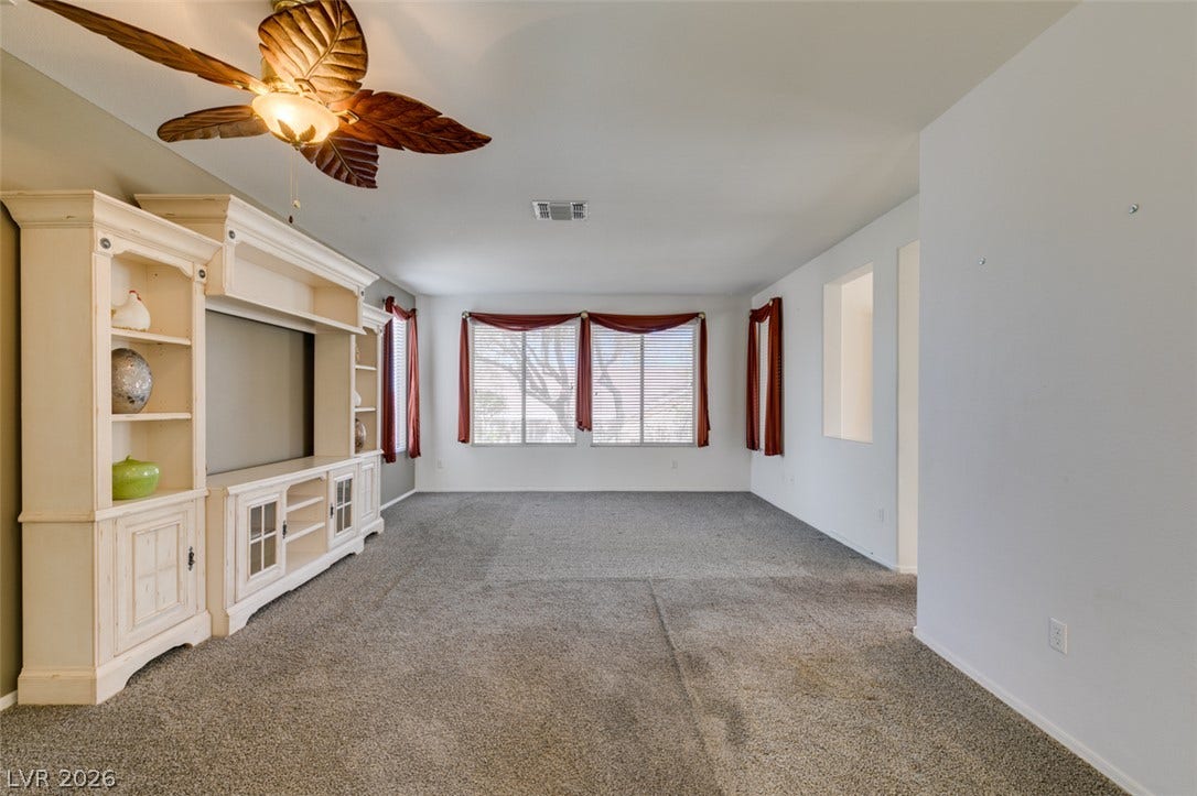 A spacious carpeted living area features custom built-in shelving and ample window light.