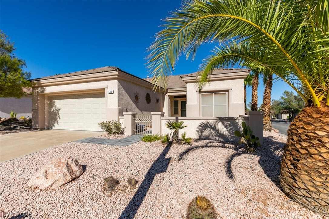 Palm trees and desert landscaping frame this classic stucco home with an attached garage.