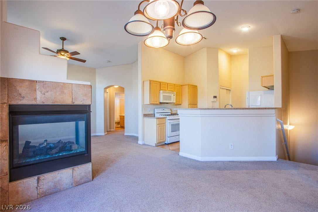 6717 Lookout Lodge Lane, #1, North Las Vegas, NV 89084 An open living space features soft carpeting, a tiled fireplace, and a raised kitchen bar.