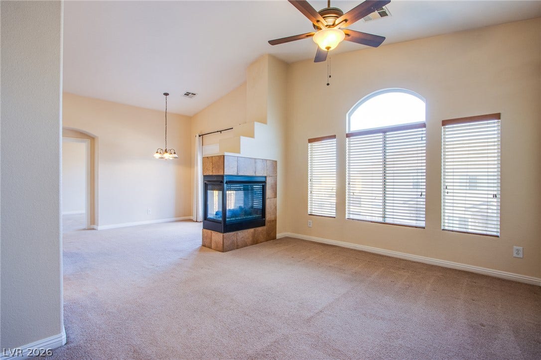 6717 Lookout Lodge Lane, #1, North Las Vegas, NV 89084 A three-sided glass fireplace anchors this vaulted living area featuring arched windows and carpeted floors.