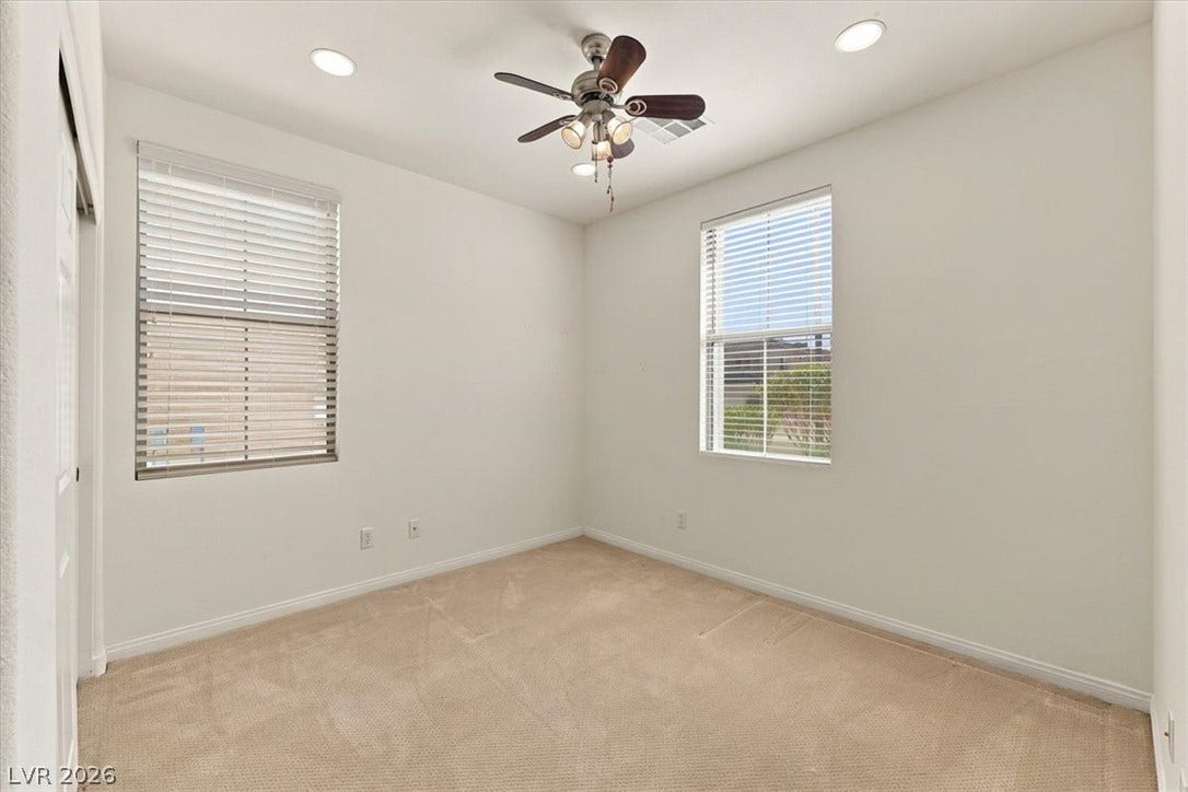 Soft carpeting pairs with neutral walls and dual windows in this quiet room.