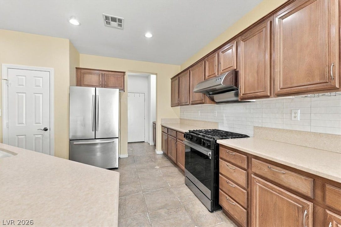 Rich wood cabinetry paired with neutral solid-surface countertops completes this functional cooking space.