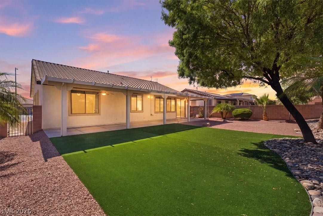 An inviting covered patio overlooks a manicured green lawn framed by mature shade trees.