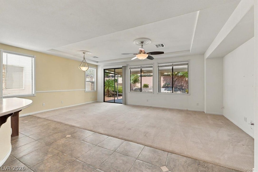 An open living space connects tile and carpet flooring under a clean tray ceiling.
