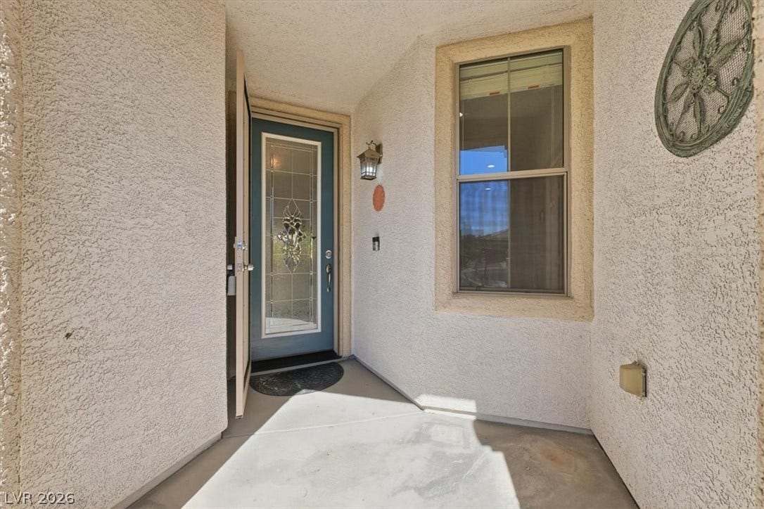An inviting recessed entry features textured stucco walls and a glass-paneled front door.