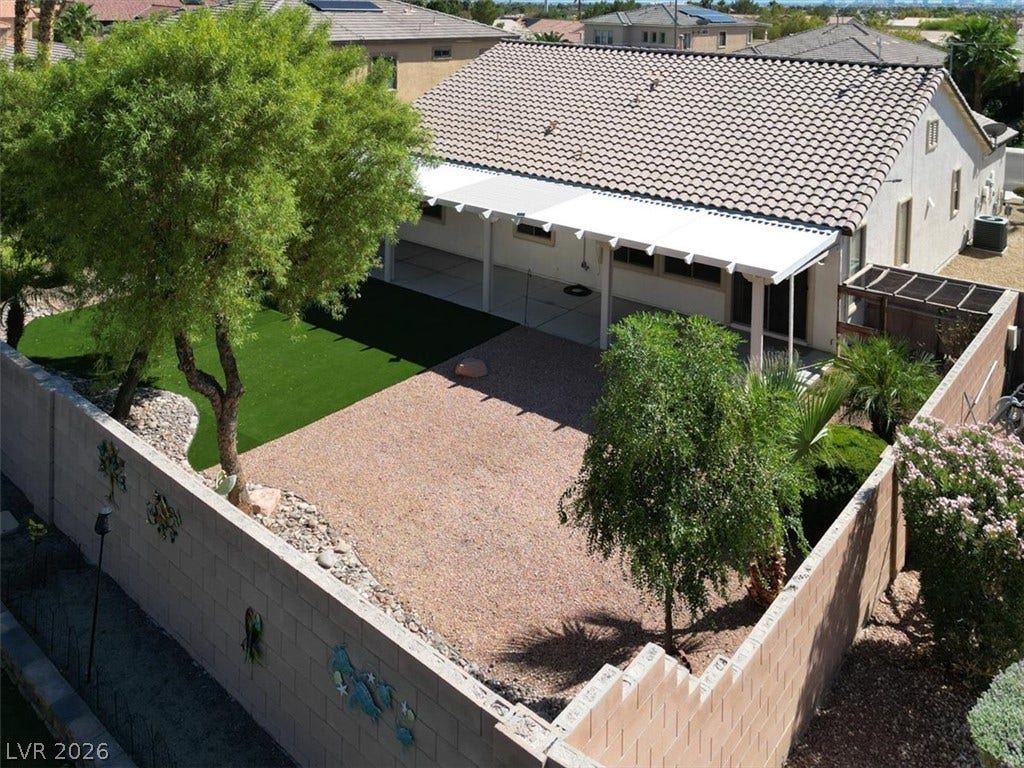 A fully enclosed backyard features low-maintenance gravel, green turf, and a long covered patio.