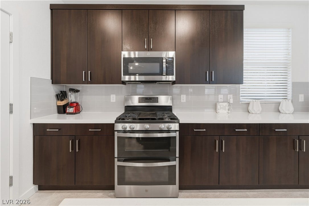 544 Front Range Lane, North Las Vegas, NV 89084 Rich dark cabinetry and solid stone countertops frame a modern stainless steel gas range.