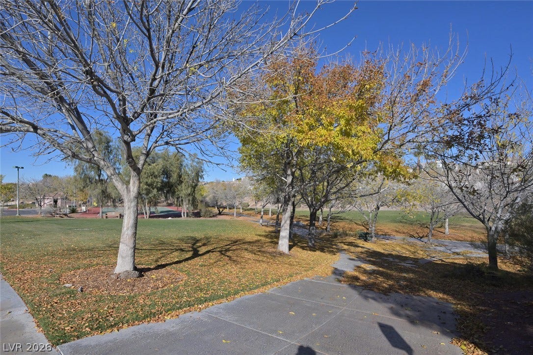 1421 Dragon Rock Drive, Henderson, NV 89052 Mature trees shade paved pathways winding through a spacious green park area under clear blue skies.