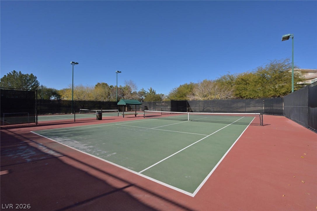 1421 Dragon Rock Drive, Henderson, NV 89052 Fenced outdoor tennis courts sit under a clear blue sky, surrounded by mature trees.