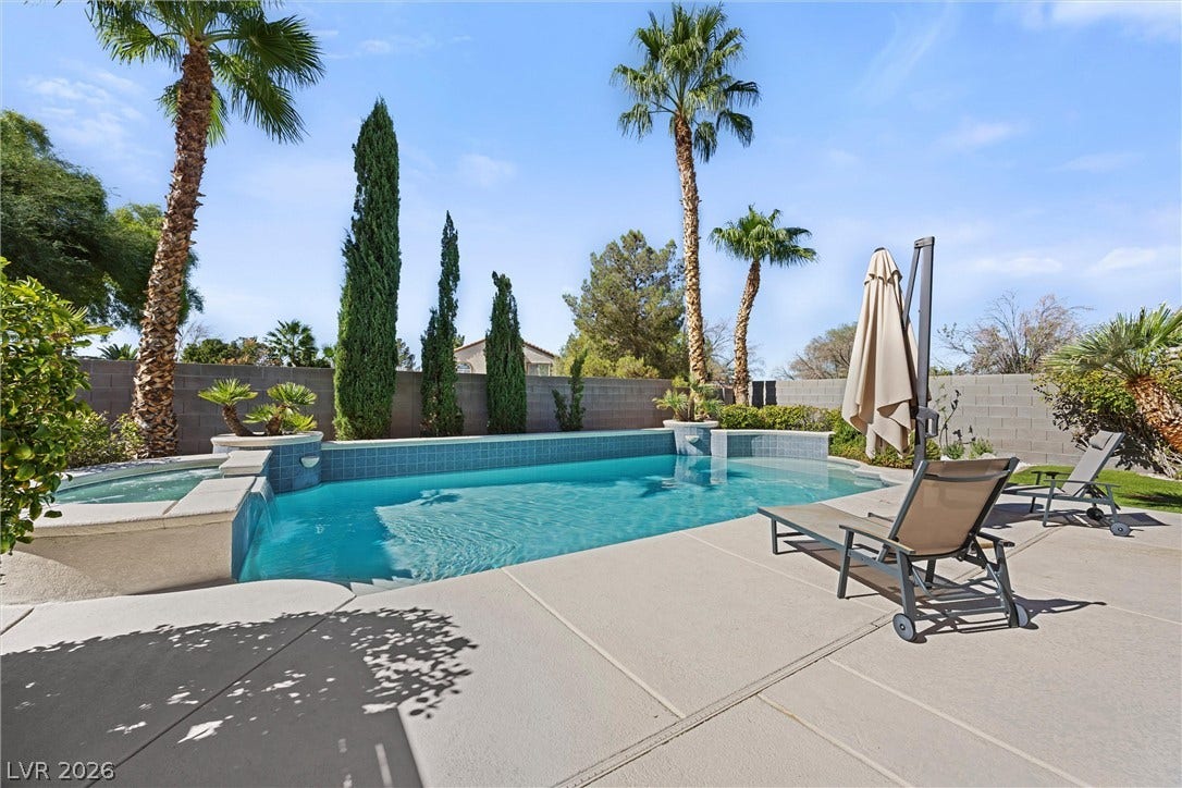 1421 Dragon Rock Drive, Henderson, NV 89052 An inviting swimming pool and integrated spa sit surrounded by a concrete patio and palm trees.