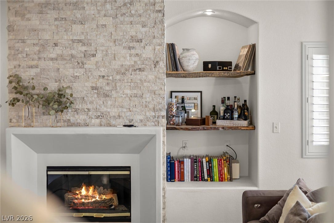 1421 Dragon Rock Drive, Henderson, NV 89052 An elegant stone-surround fireplace complements integrated shelving within a light-filled living area.