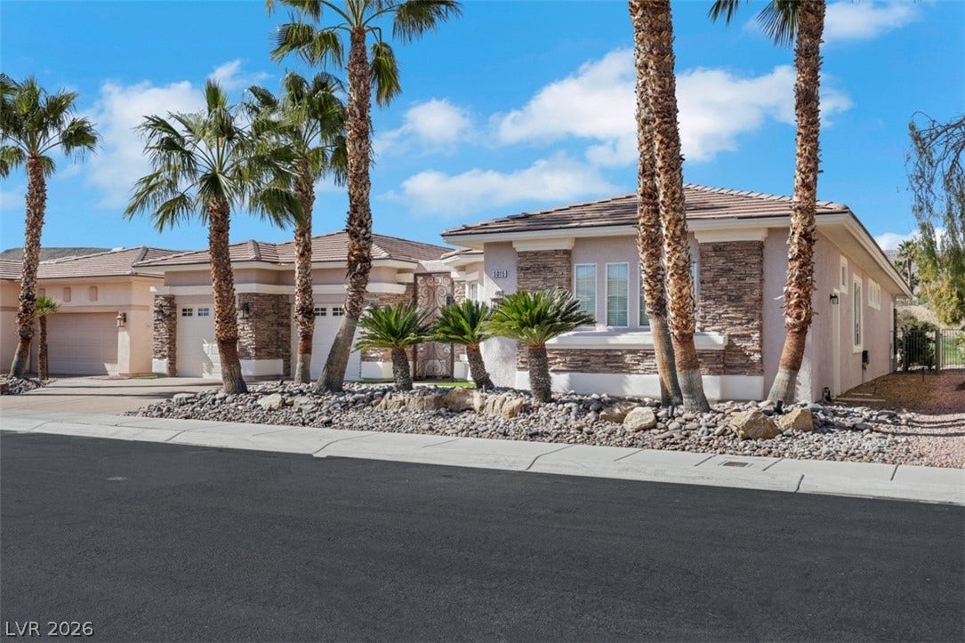 5015 Rivedro Street, Las Vegas, NV 89135 Stately palm trees and stone accents frame this desert-landscaped ranch home under blue skies.