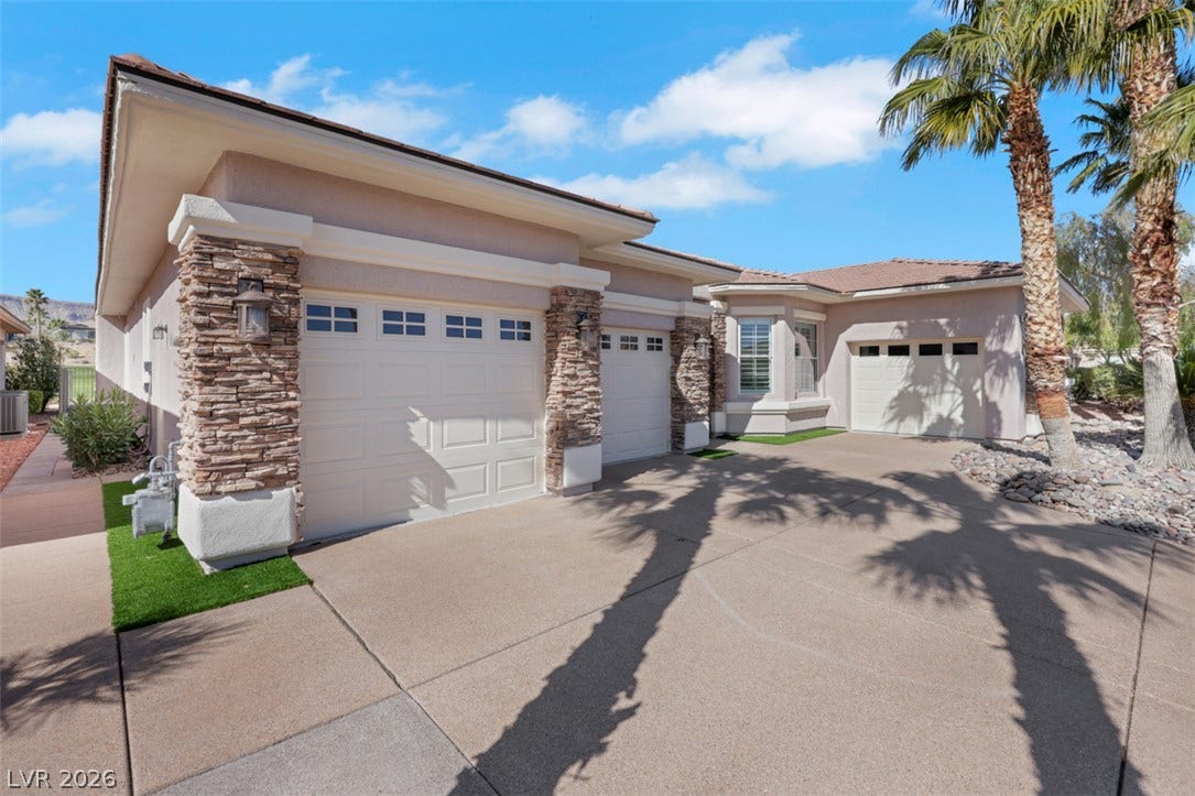 5015 Rivedro Street, Las Vegas, NV 89135 Stacked stone accents frame the spacious garages set alongside a wide, paved driveway.