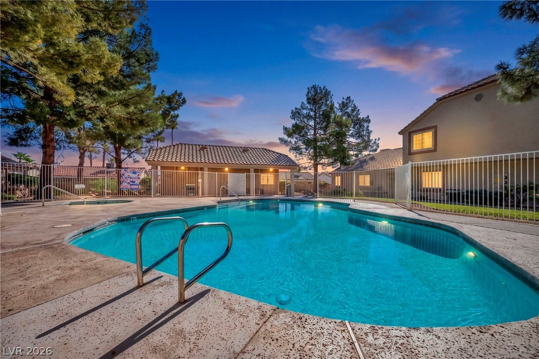 Mature trees frame a sparkling community pool and spa area enclosed by protective fencing.