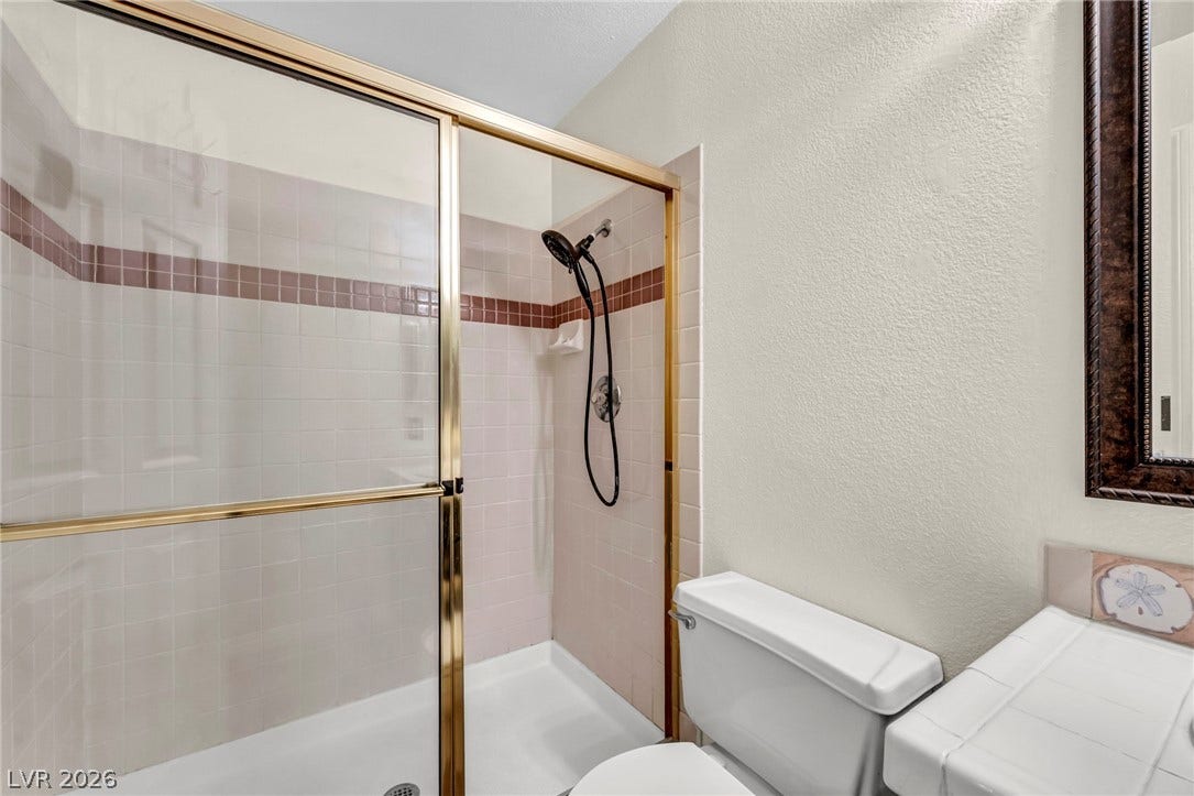 Tiled walk-in shower features gold-trimmed sliding glass doors next to a tiled vanity.