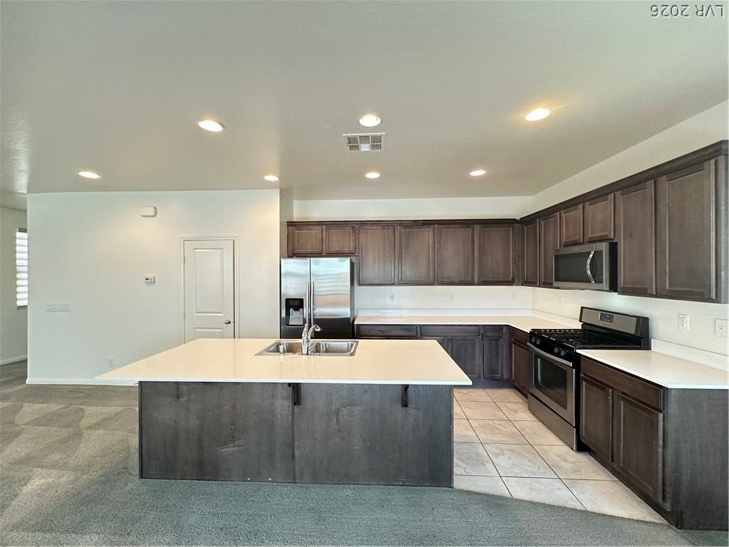 Rich cabinetry contrasts beautifully with clean countertops and tile flooring in this open-concept kitchen.