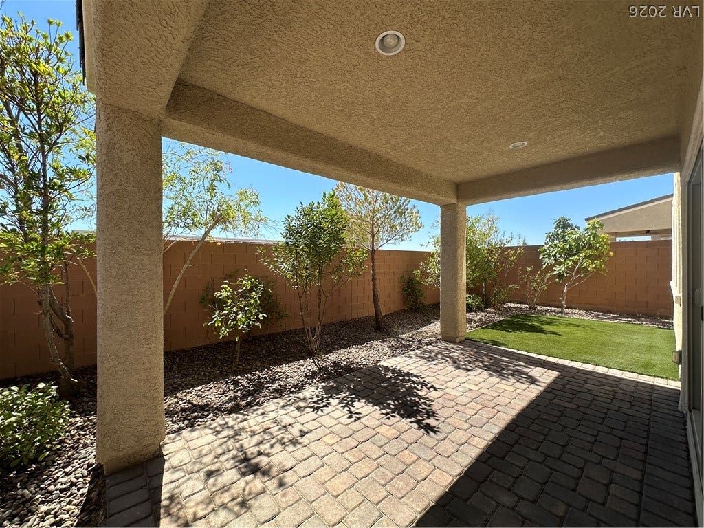 A covered patio overlooks a private paved backyard shaded by mature trees.
