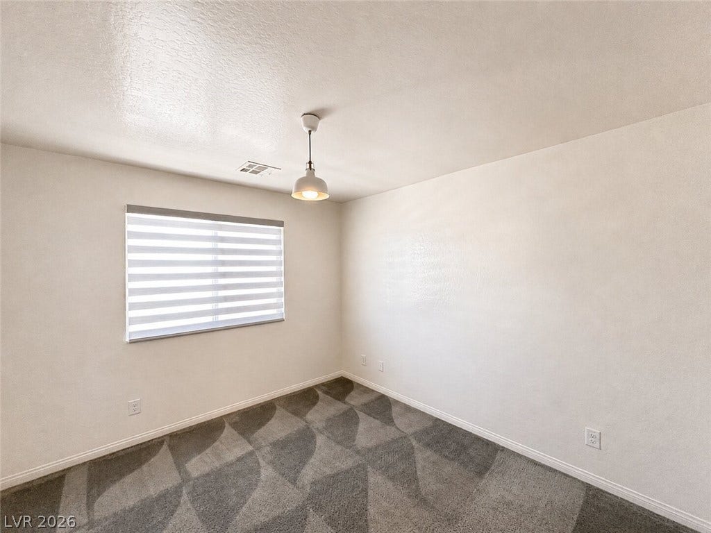 Patterned carpeting and a single window define this versatile secondary bedroom space.