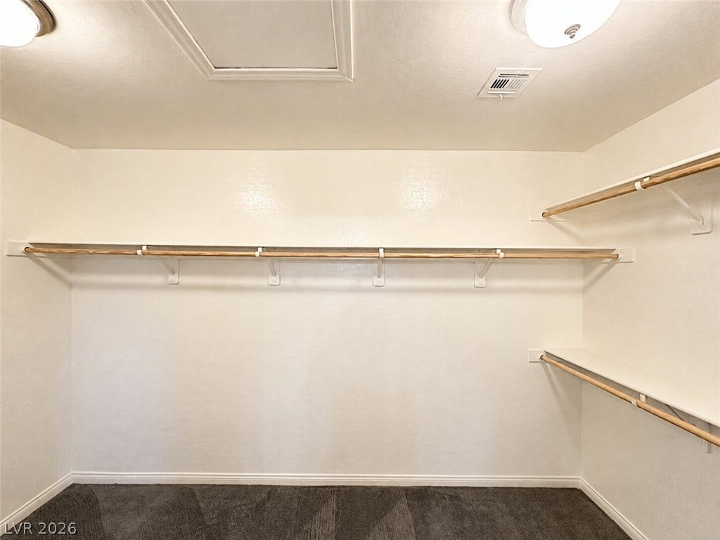 A spacious walk-in closet includes ample shelving and carpeted flooring.