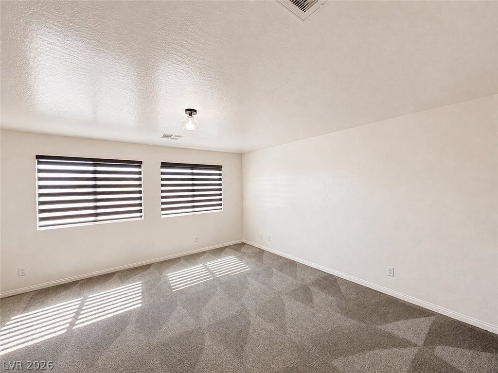 Plentiful natural light filters through dual windows onto soft neutral carpeting.