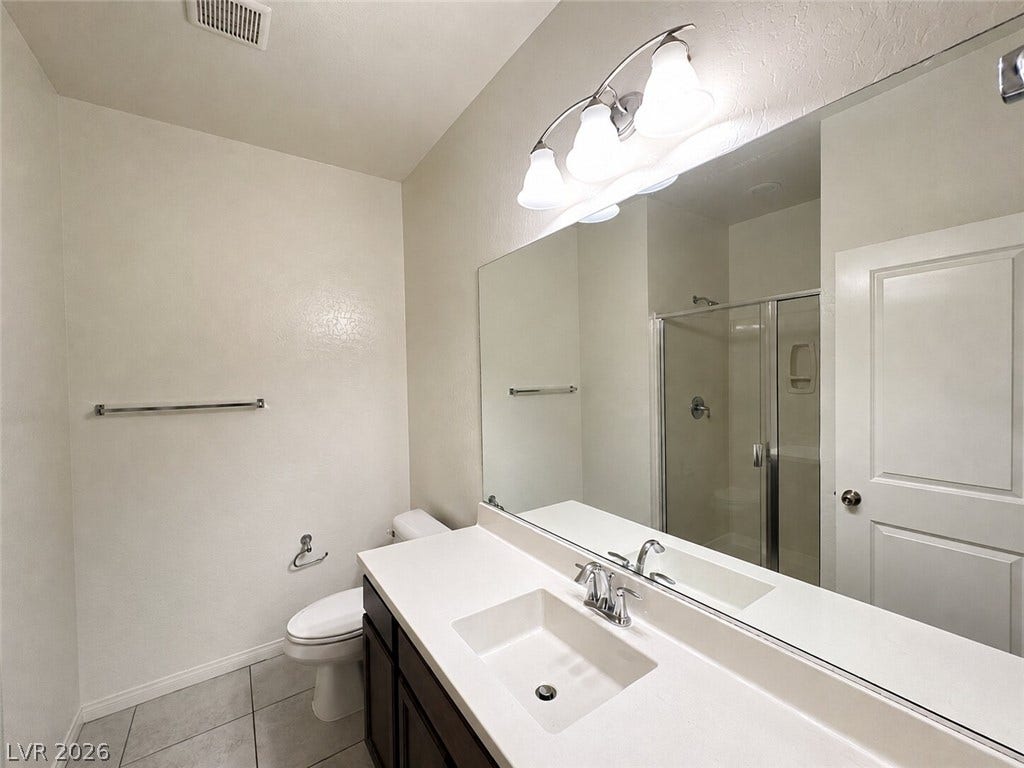 Tiled flooring and a modern vanity with a large mirror define this clean bathroom space.
