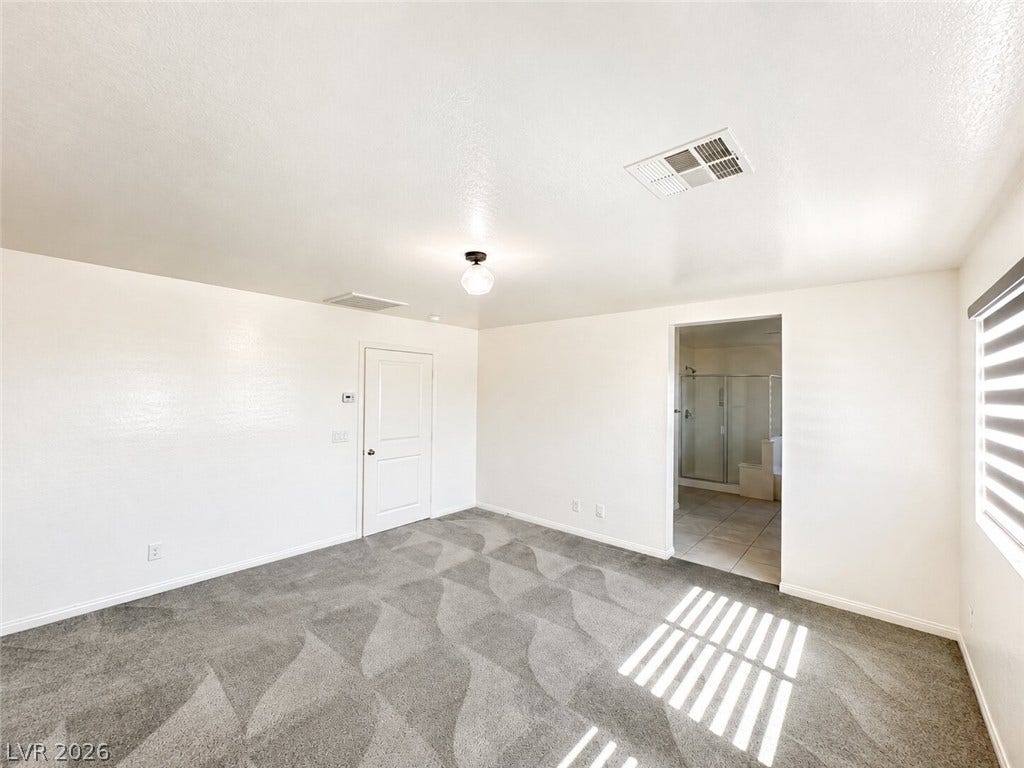 Patterned carpeting and high ceilings define this spacious bedroom leading into an attached bath.