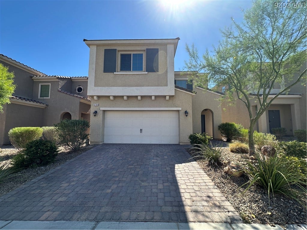 A paved driveway leads to the attached garage of this two-story stucco home.