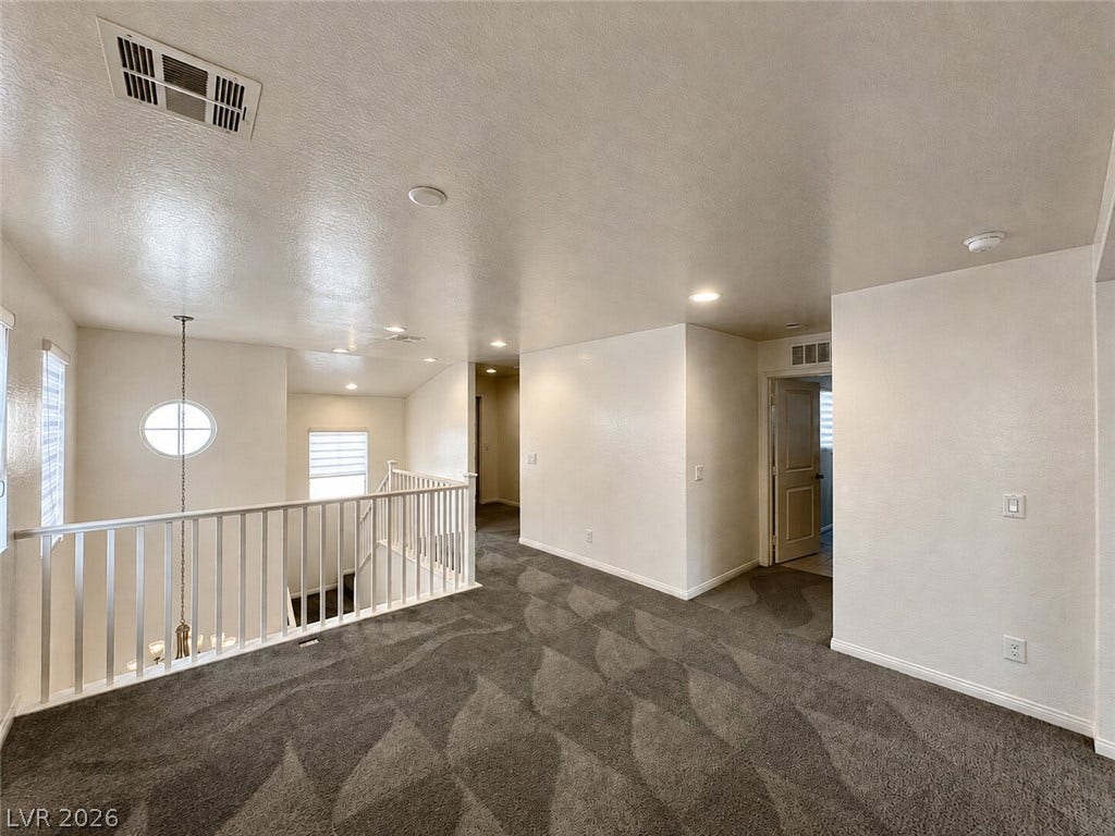 An airy upper-level landing overlooks the lower floor beneath a neutral vaulted ceiling.