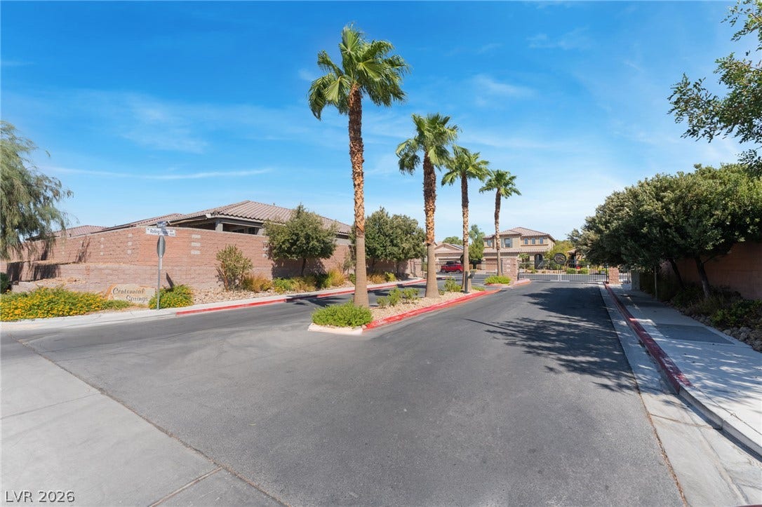 Gated neighborhood entrance lined with towering palm trees under a bright blue sky.