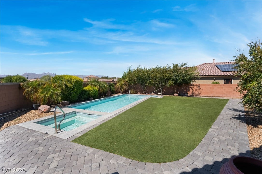 An inviting swimming pool and integrated spa sit alongside a lush green lawn area.