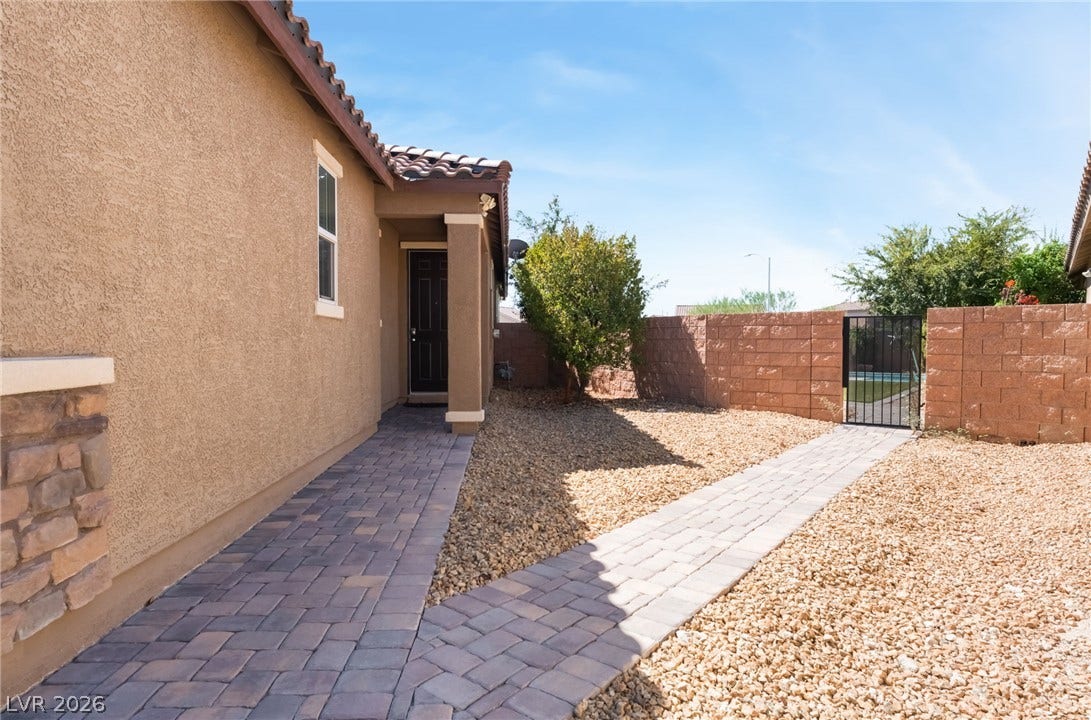 Paver walkways wind through low-maintenance desert landscaping alongside stucco and stone veneer exterior walls.