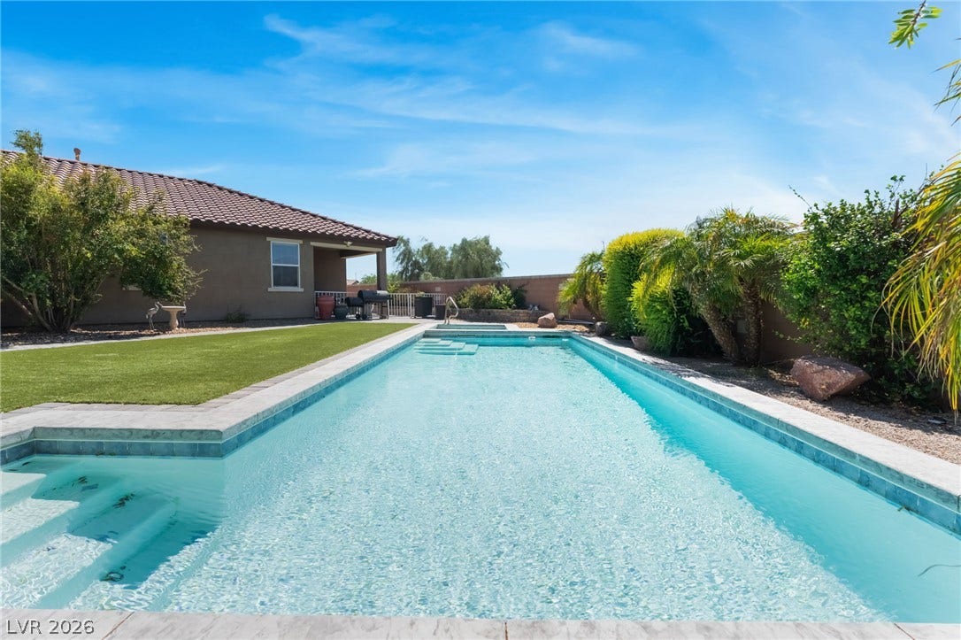 A sparkling swimming pool anchors the backyard alongside a neat lawn and mature palm trees.