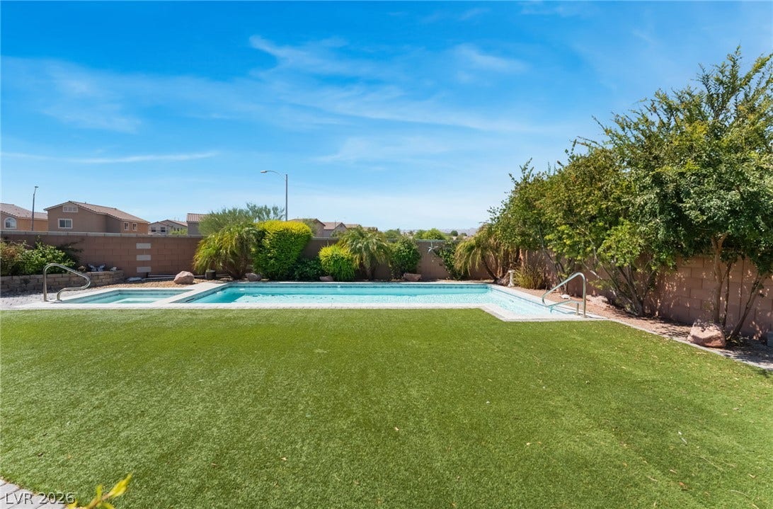 Lush artificial turf frames a sparkling in-ground pool and integrated spa under clear desert skies.