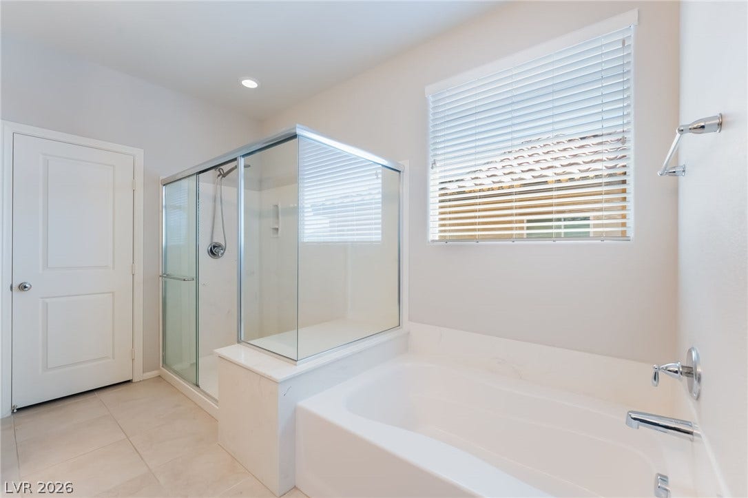 A glass-enclosed shower stands alongside a deep soaking tub beneath a naturally lit window.