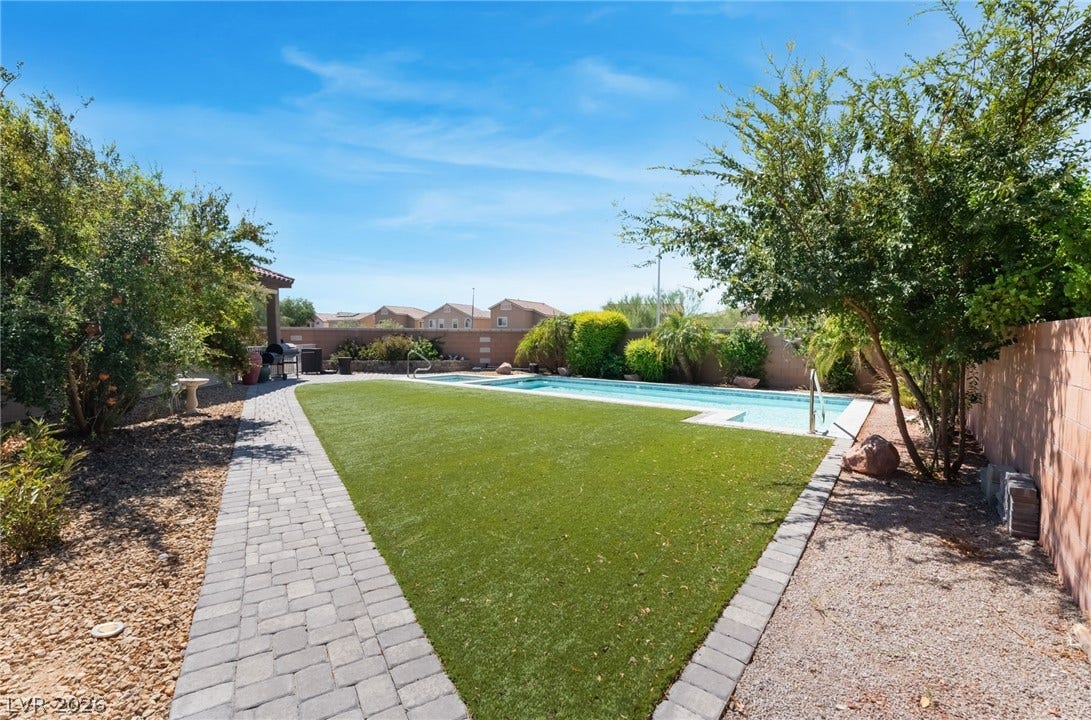 Manicured lawns and stone paver pathways line this private backyard oasis with a refreshing pool.