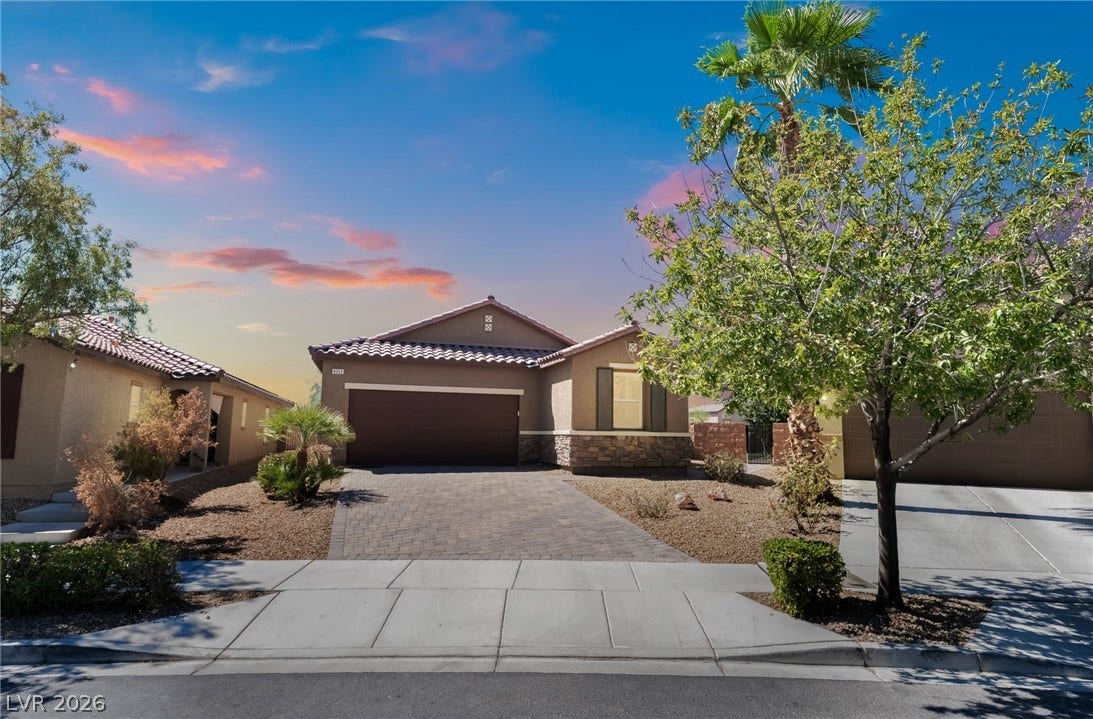 A paved driveway leads to a single-story home featuring a tile roof and stone accents.