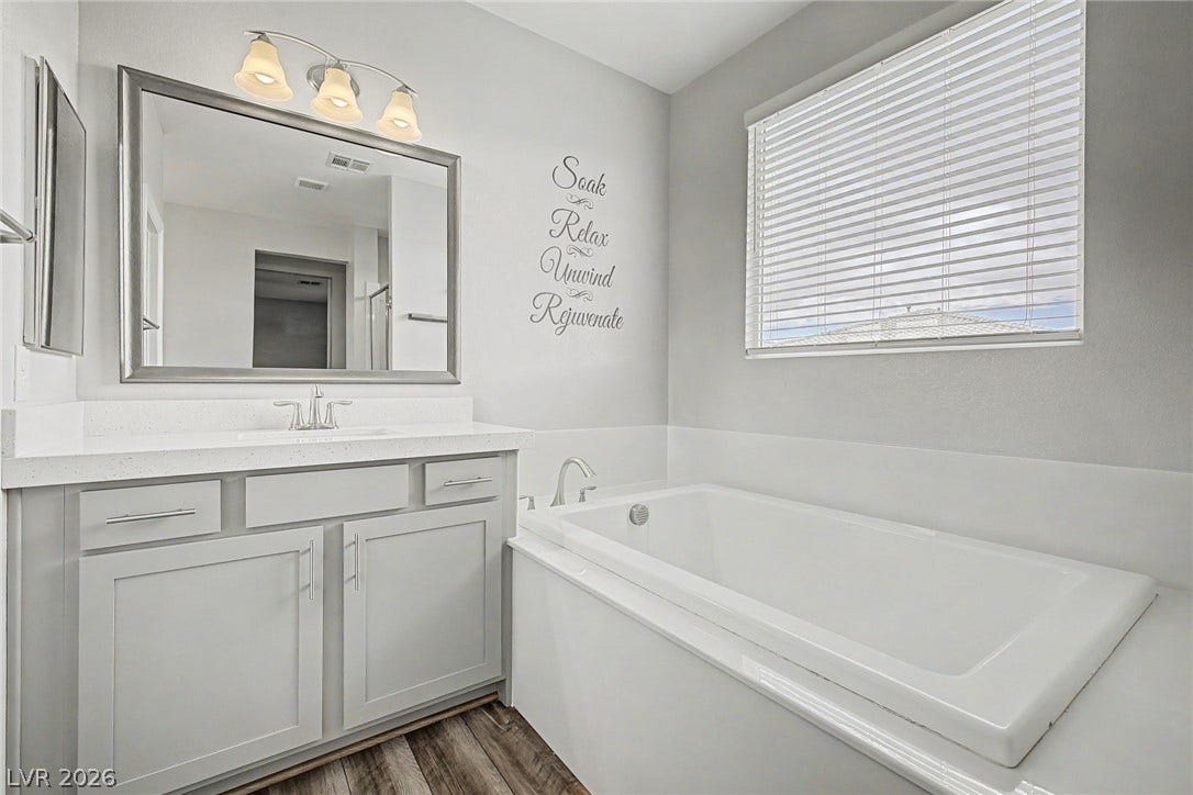 4618 Summer Azure Street, North Las Vegas, NV 89031 A deep soaking tub sits adjacent to a classic single vanity on wood-look flooring.