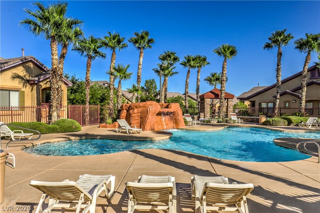 8250 N Grand Canyon Drive, #1006, Las Vegas, NV 89166 Palm trees surround a resort-style swimming pool featuring a rock waterfall and sun-drenched concrete decking.