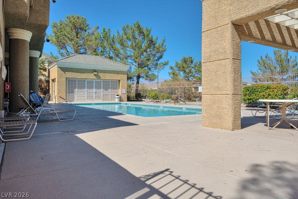 A sparkling community pool sits framed by stucco pillars and sun-drenched concrete decking.