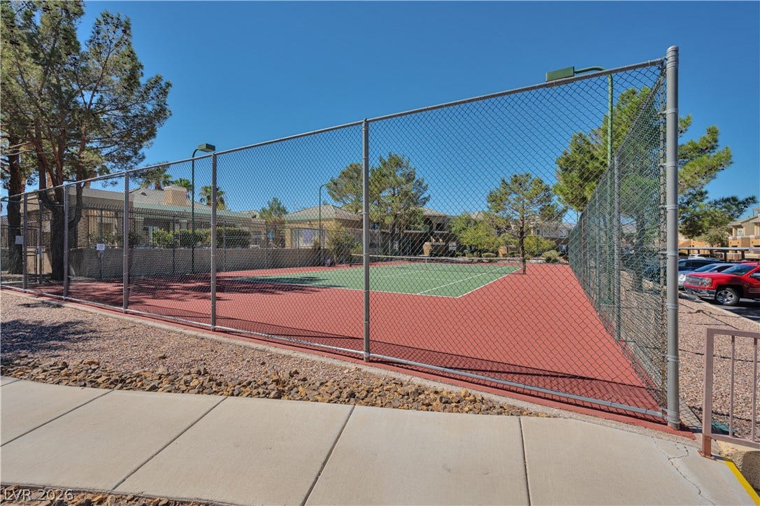 A well-maintained community tennis court is fully enclosed by chain-link fencing.