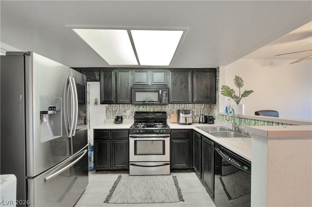 Dark cabinetry and stainless steel appliances anchor this kitchen workspace under recessed panel lighting.