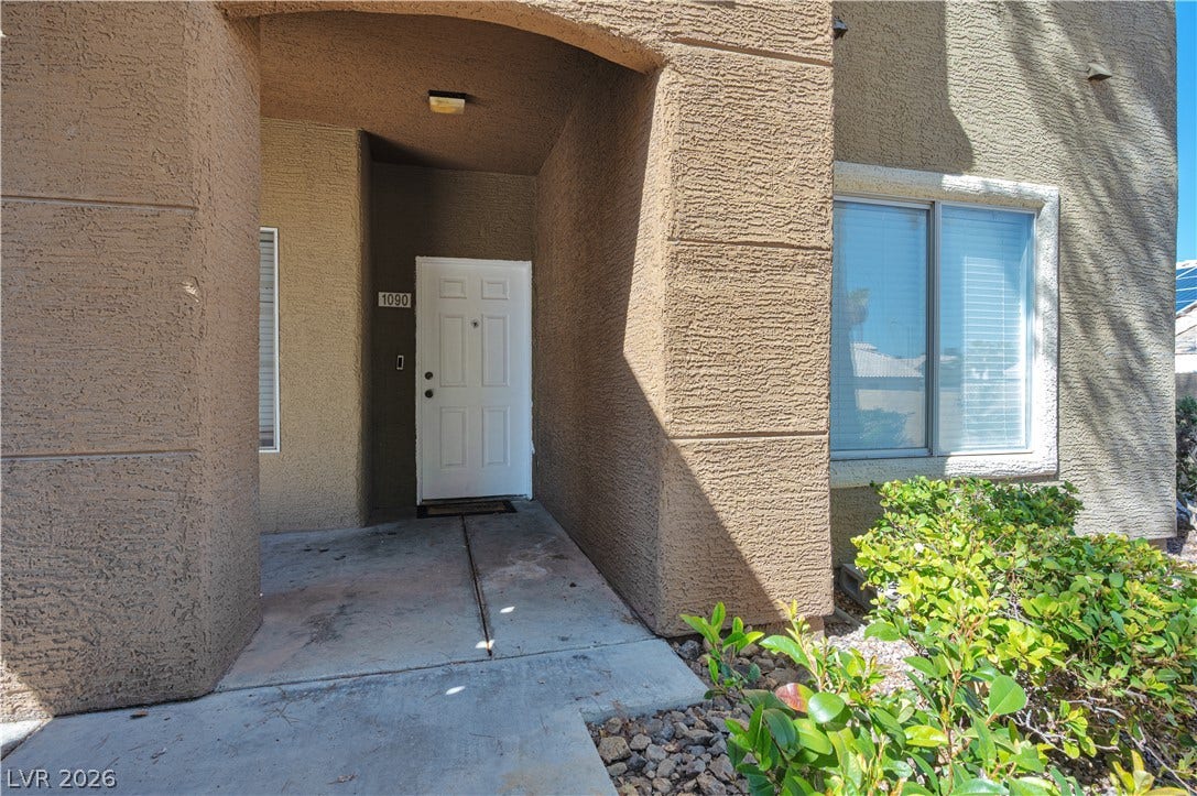 An arched entry way leads to the private front door framed by stucco exterior walls.